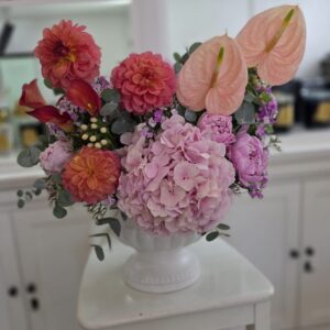🌸 סידור אביבי בכלי קרמיקה אלגנטי 🌸 סידור פרחים עשיר ומעודן שמשלב הרמוניה של צבעים – הורודים הרכים של הידרנג'ה ופתני האנתוריום, לצד נגיעות עזות של דליה וקלות בורדו. הכול מסודר בכלי קרמיקה לבן עם רגל, המוסיף נופך קלאסי ומרשים. מושלם כמתנה לאירועים, ימי הולדת או להאיר כל חלל בבית.