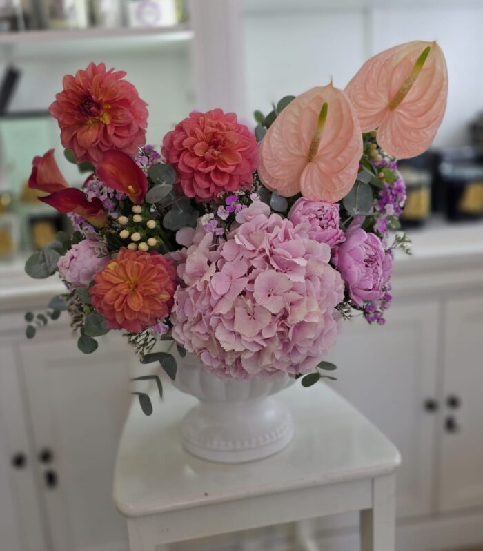 🌸 סידור אביבי בכלי קרמיקה אלגנטי 🌸 סידור פרחים עשיר ומעודן שמשלב הרמוניה של צבעים – הורודים הרכים של הידרנג'ה ופתני האנתוריום, לצד נגיעות עזות של דליה וקלות בורדו. הכול מסודר בכלי קרמיקה לבן עם רגל, המוסיף נופך קלאסי ומרשים. מושלם כמתנה לאירועים, ימי הולדת או להאיר כל חלל בבית.